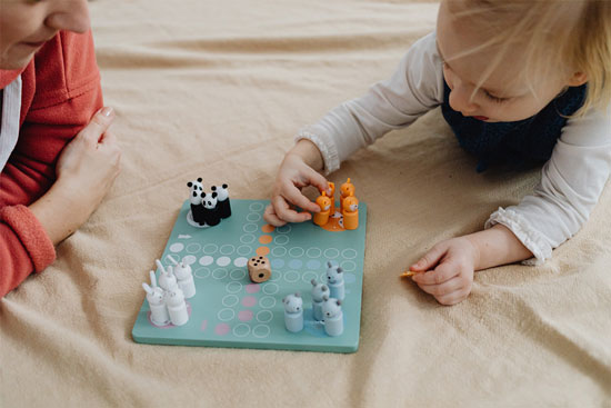 a young girl playing small foot ludo with her mother