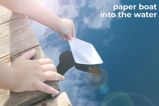 little boy releases paper boat into the water
